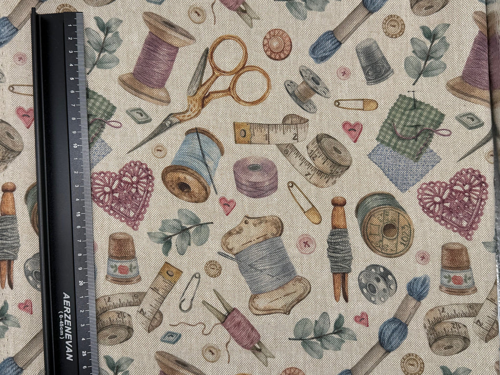 Fabric with sewing-themed pattern including spools of thread, scissors, and thimbles on a beige background.
