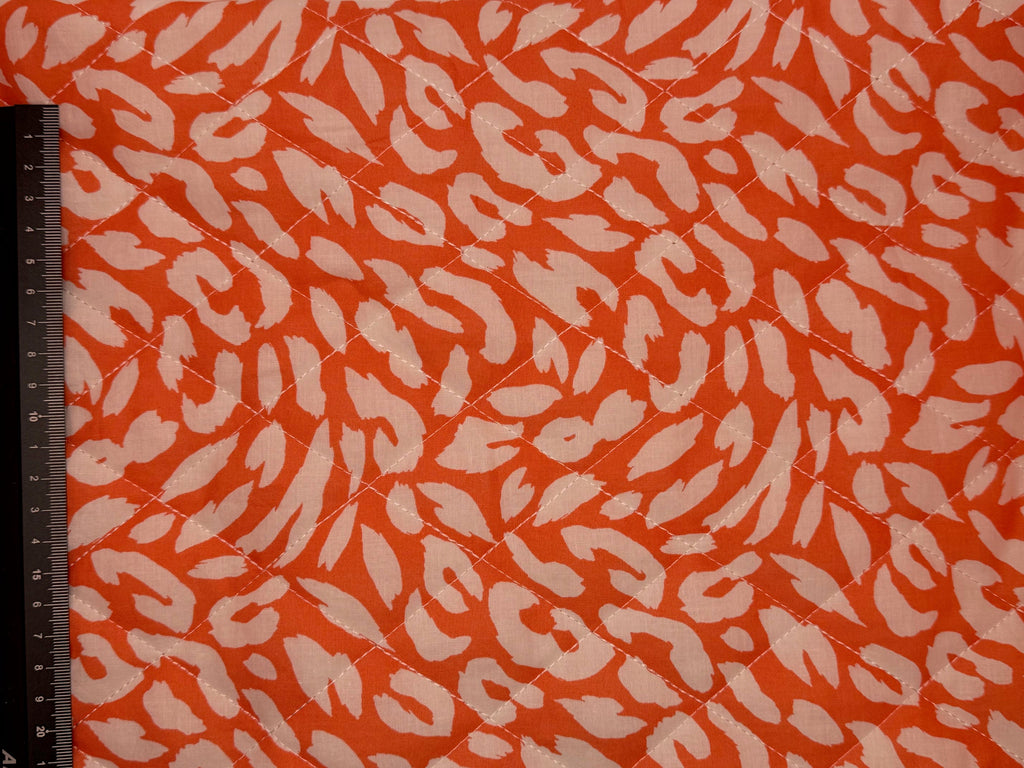 Fabric with a animal print pattern on an orange background, measured by a ruler.
