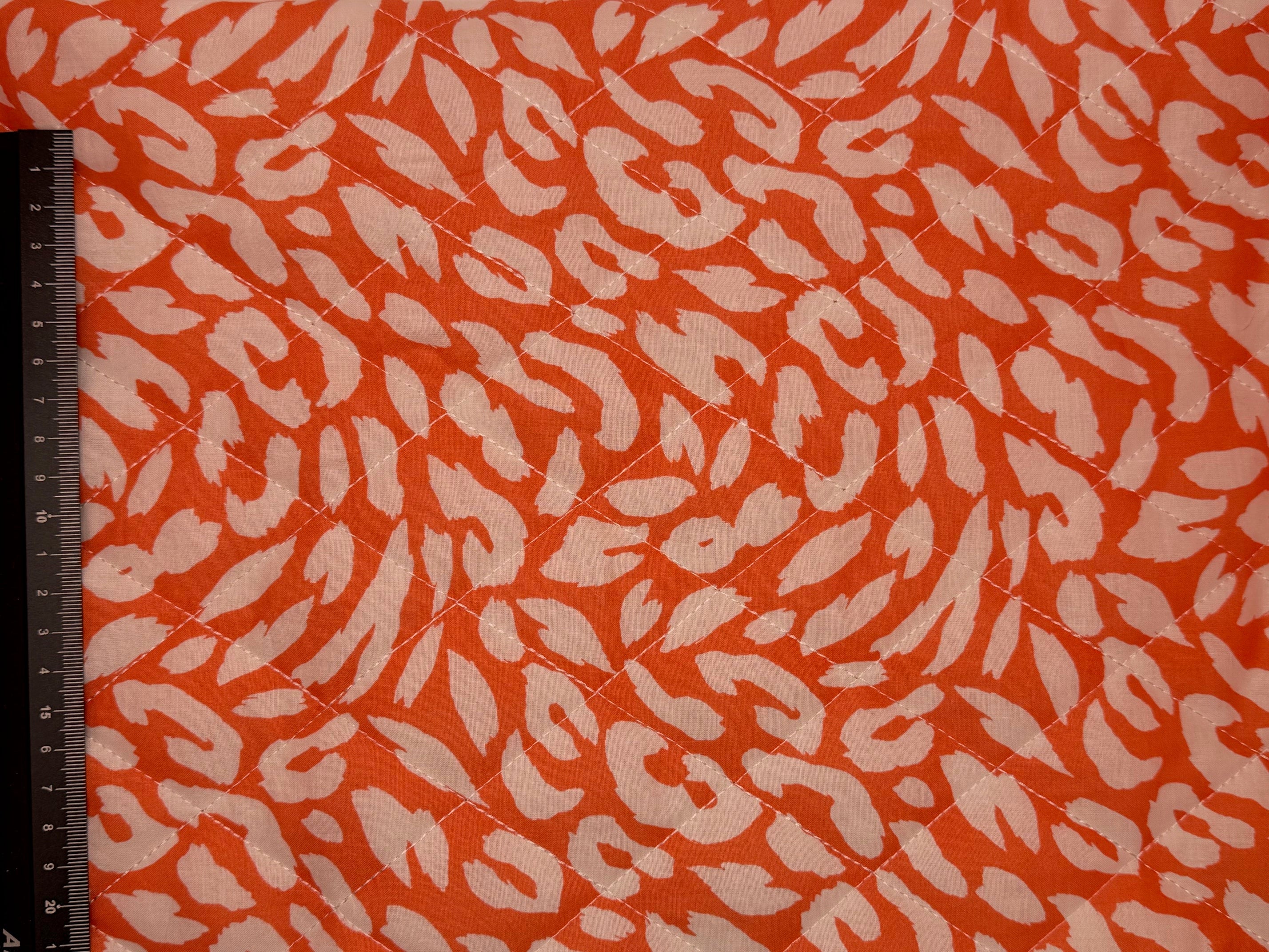 Fabric with a animal print pattern on an orange background, measured by a ruler.