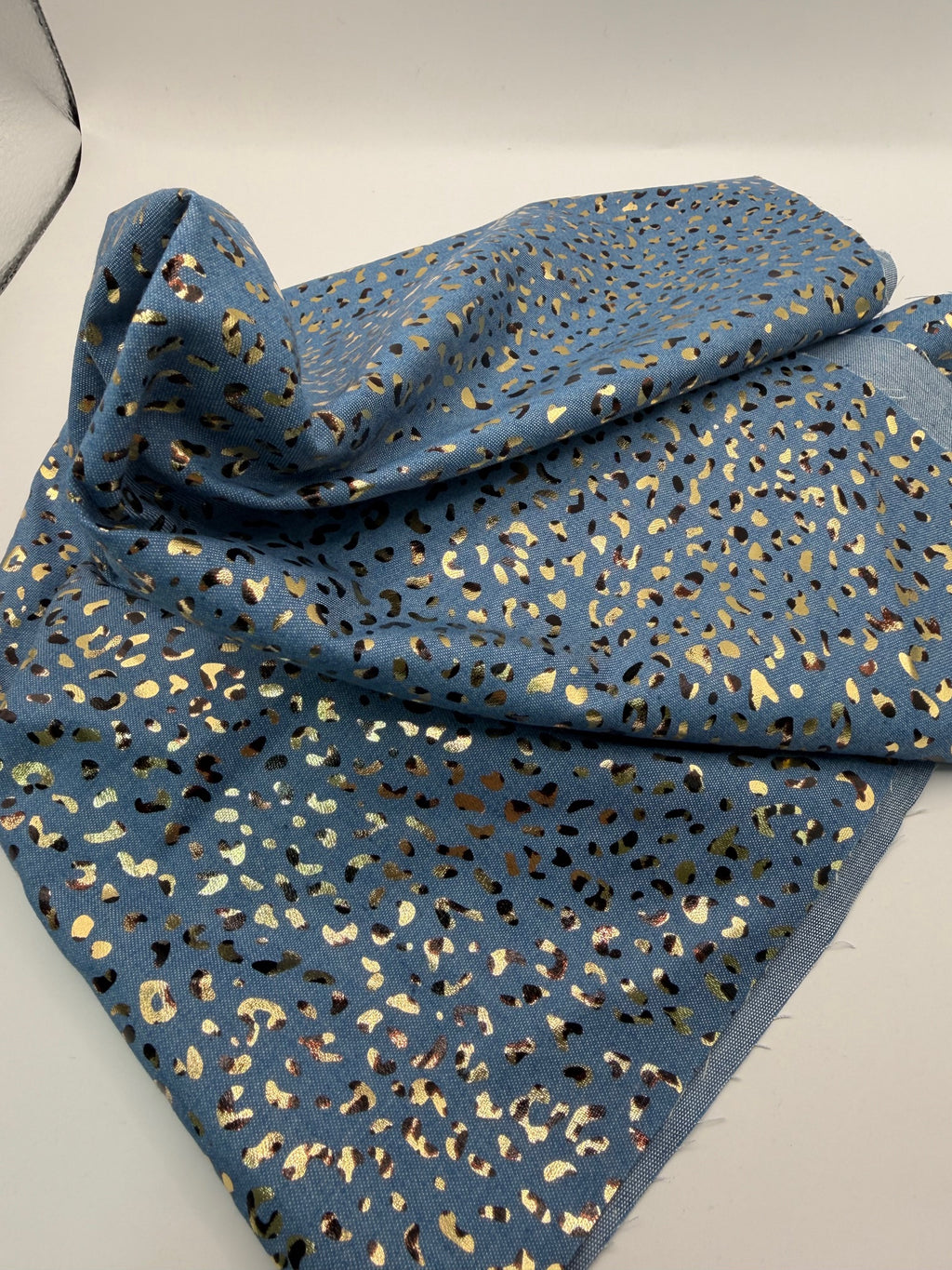 Folded blue fabric with gold and black pattern on a light gray background