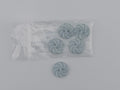 Four small round spiral-shaped buttons in a pale blue-gray color, with one button placed to the left of a clear plastic bag containing the remaining three buttons.
