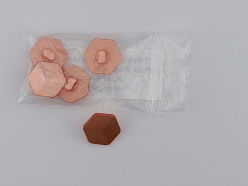A clear plastic bag containing four faceted peach-pink hexagonal pieces with small tabs, alongside one matching brown hexagonal piece on a light gray background.