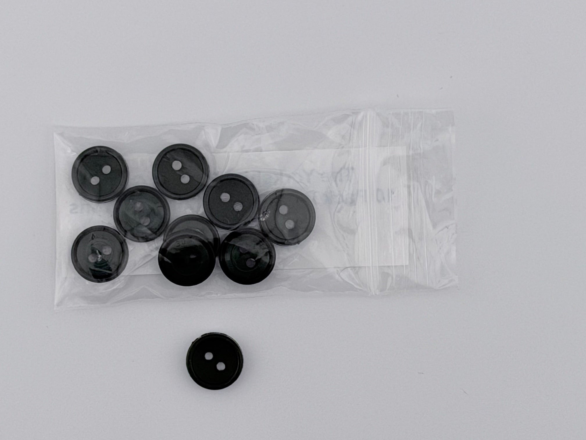 Dark Green plastic buttons, including one loose button and a clear plastic bag containing eight more, displayed on a light gray background.